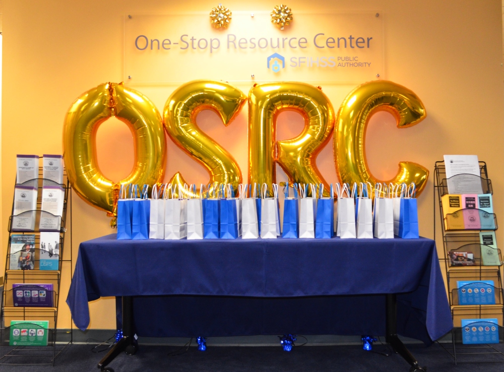 Photo inside of the One-Stop Resource Center with a table of bagged gifts and celebration balloons spelling out OSRC.