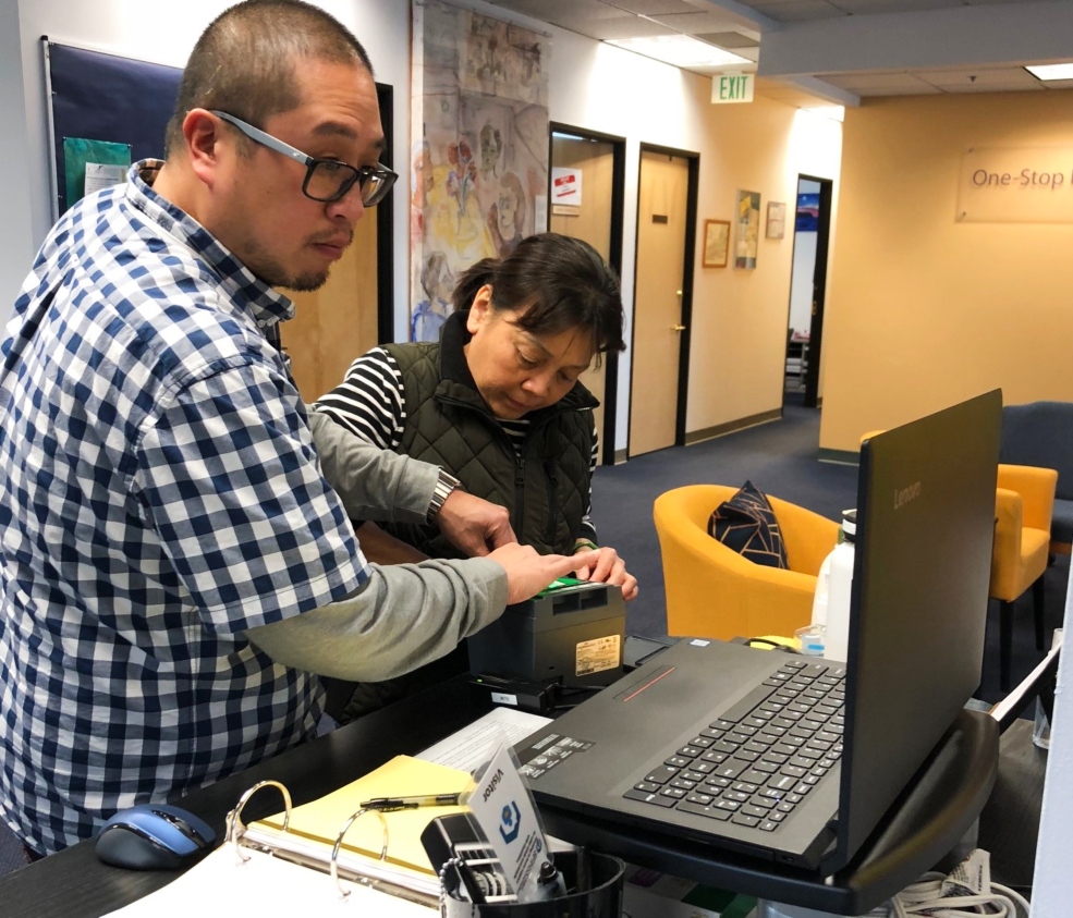 Photo of a man asisting a female provider in receiving a LiveScan fingerprinting.