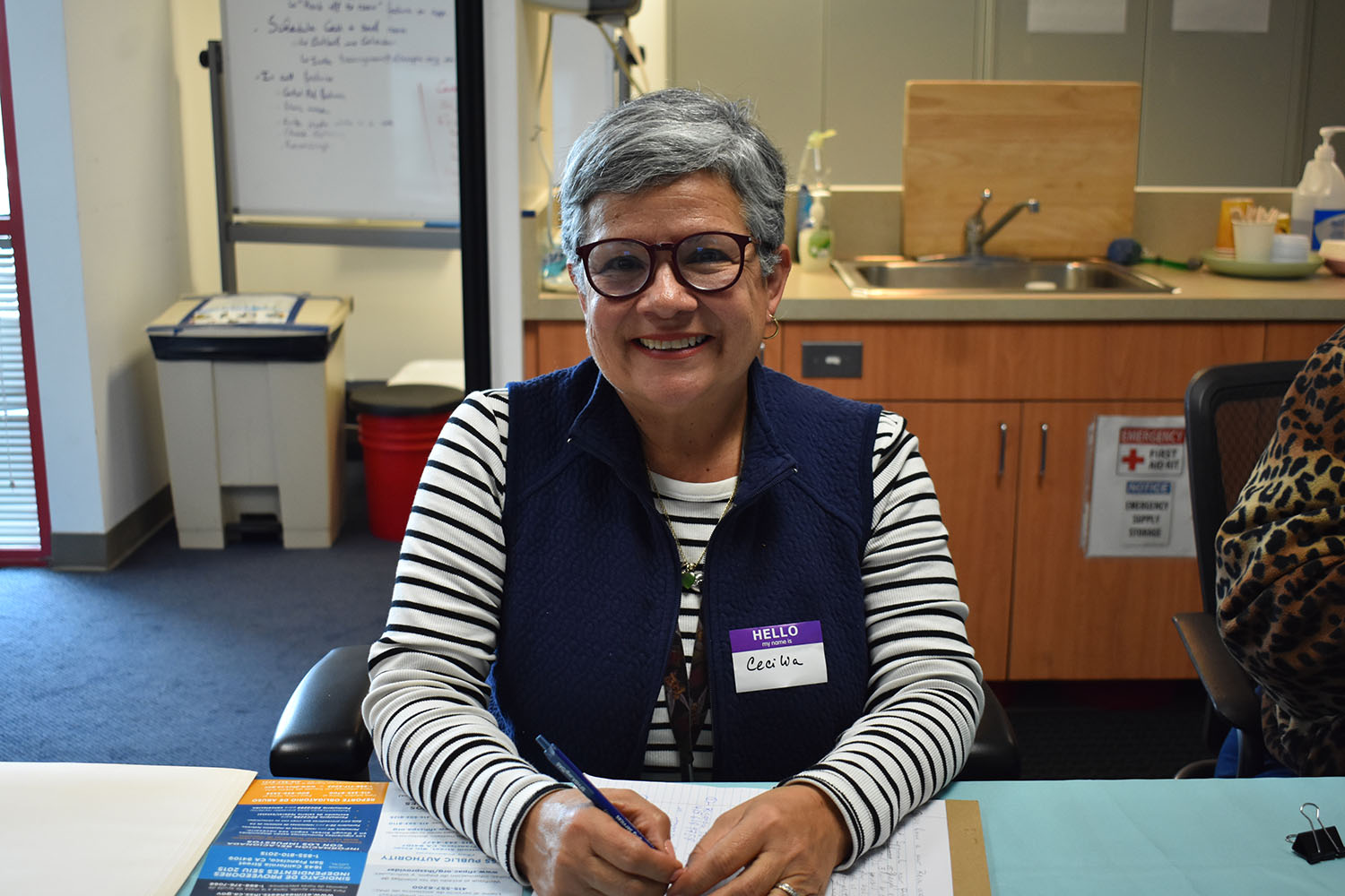 Photo of an older woman smiling and volunteering at a registration table to help with recruit new providers.