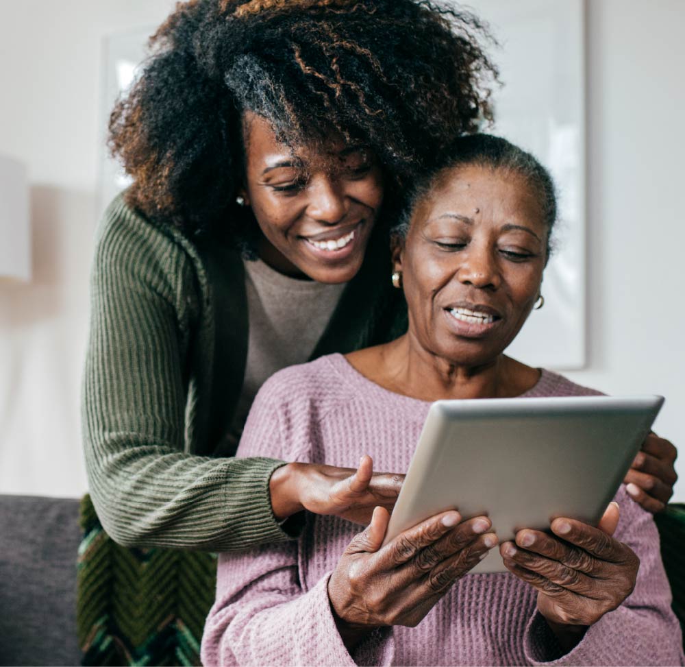Photo of an adult daughter assisting her mother with a digital tablet.