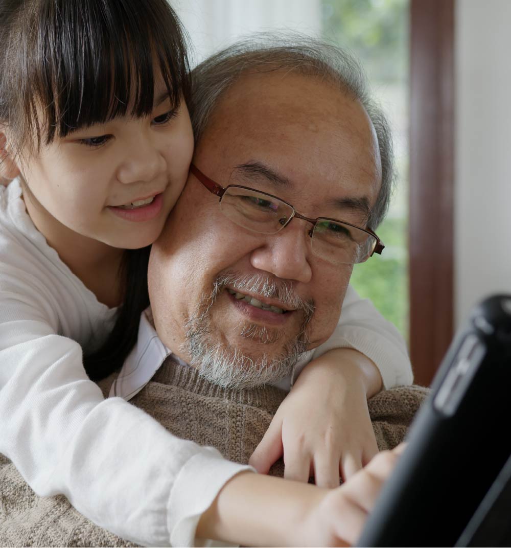 Photo of a young granddaughter looking over the shoulder of her grandfather with a digital tablet.