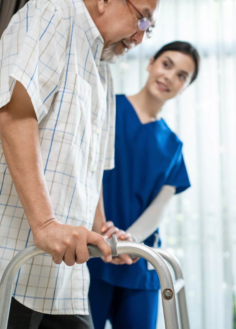 Photo of an older man with a walker being assisted by a young female care provider.